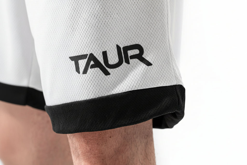 Close-up of a white sports jersey with black trim and 'TAUR' logo on a person wearing it.