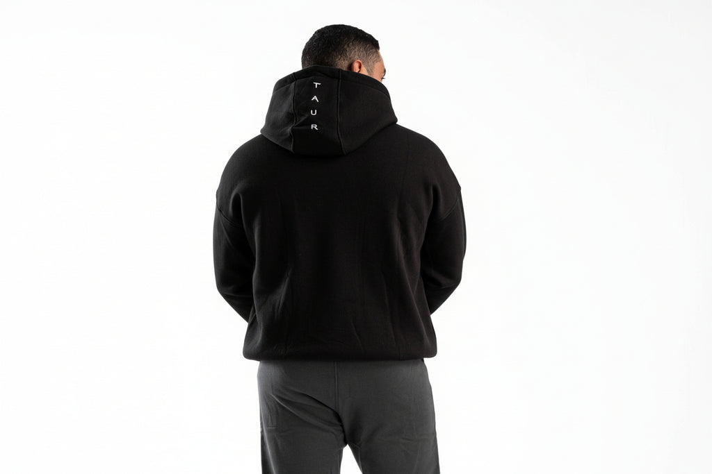 Person wearing a black hoodie with a brand logo on the back, standing against a white background