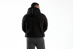 Person wearing a black hoodie with a brand logo on the back, standing against a white background