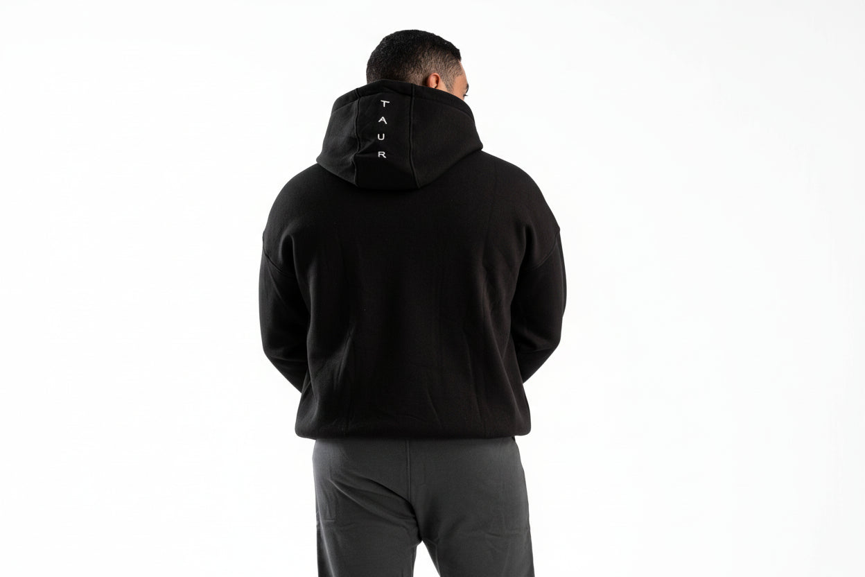 Person wearing a black hoodie with a brand logo on the back, standing against a white background