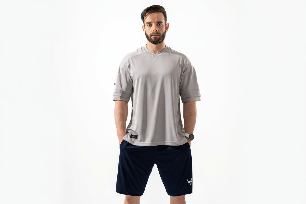 Man wearing a gray athletic shirt and navy shorts on a white background