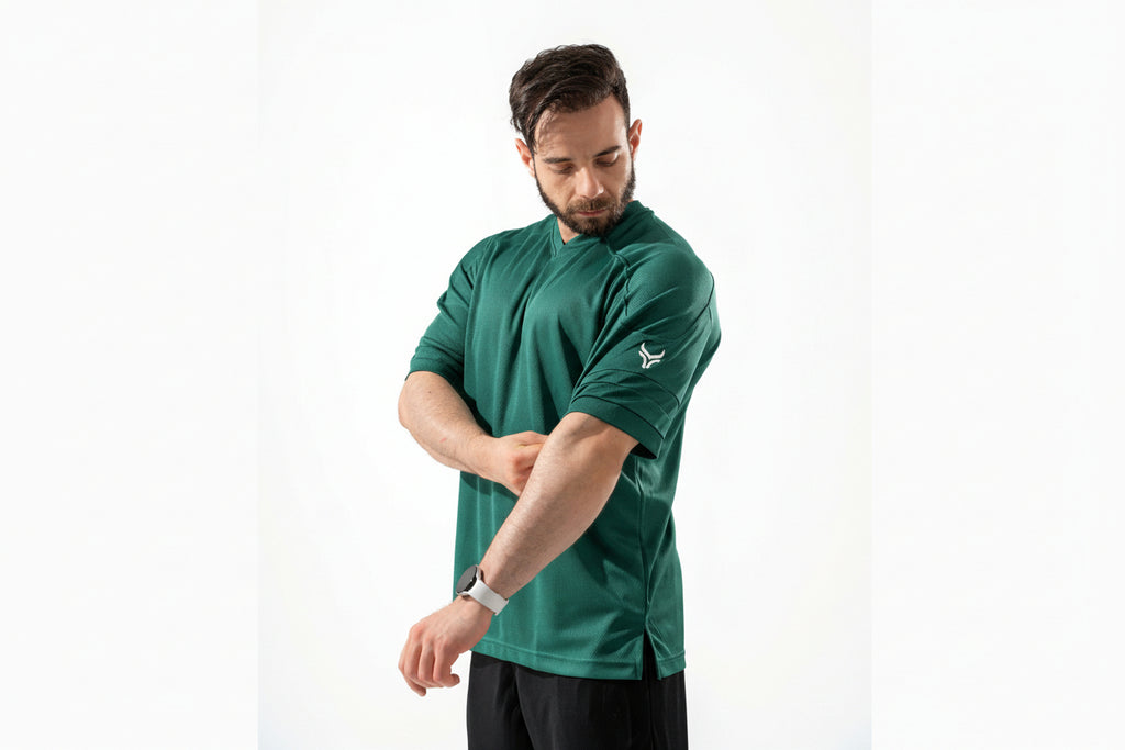 Man wearing a green athletic shirt with a logo on a white background

