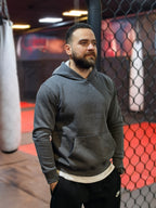 Man wearing a gray hoodie in a boxing ring setting

