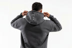 Person wearing a gray hoodie with a brand logo on the back, standing against a white background

