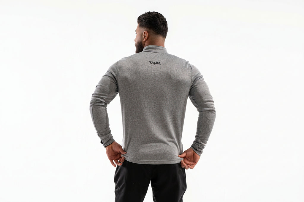 Man wearing a gray long-sleeve athletic shirt with a brand logo on the back, standing against a white background.