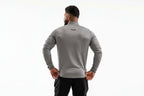 Man wearing a gray long-sleeve athletic shirt with a brand logo on the back, standing against a white background.