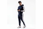 Man wearing a navy tracksuit with white accents on a white background

