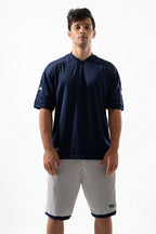 Man wearing a navy blue sports jersey and gray shorts on a white background

