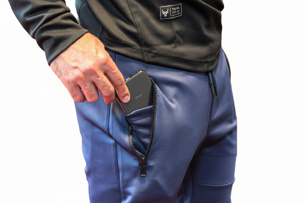 Person wearing blue pants with a zipper pocket, holding a phone.

